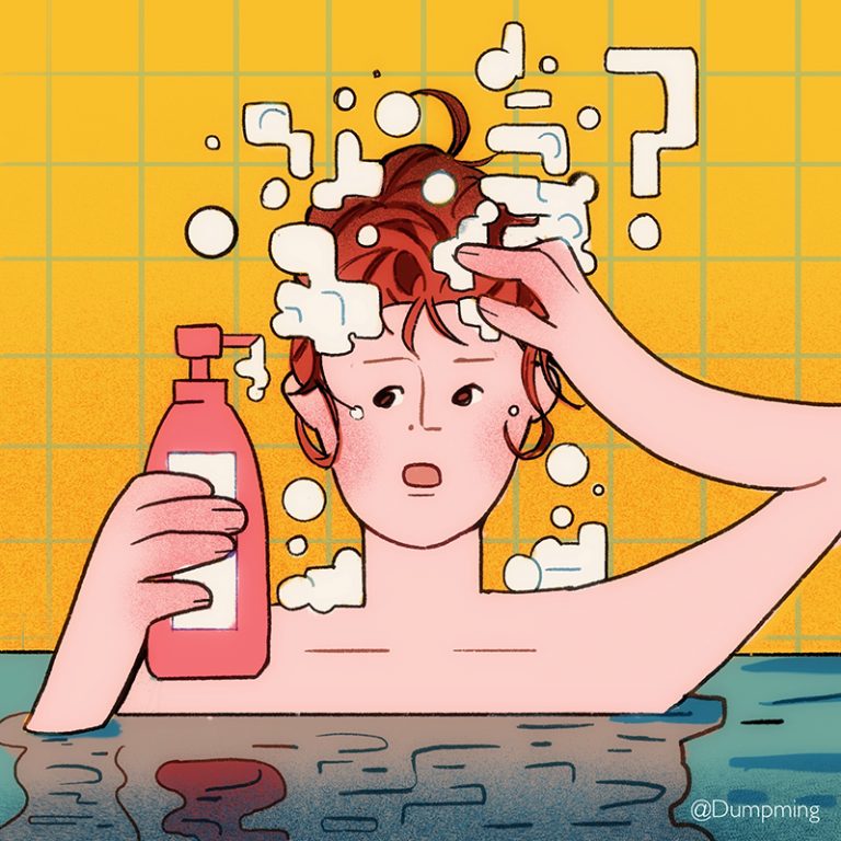 A person in the bath tub holding a bottle of shampoo in one hand and lattering the shampoo with the other.