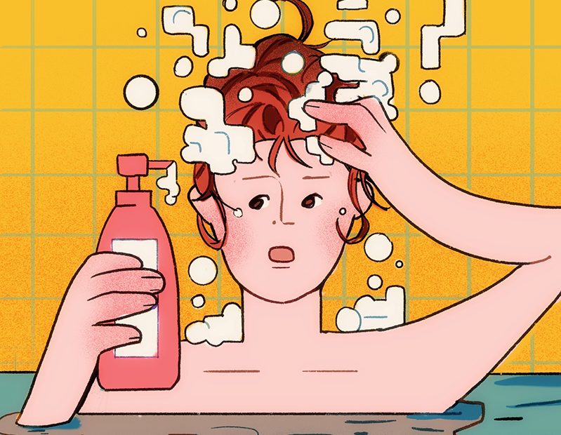 A person in the bath tub holding a bottle of shampoo in one hand and lattering the shampoo with the other.